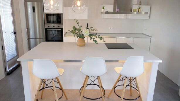 Una cocina moderna con una isla central, taburetes de bar, luces colgantes y electrodomésticos integrados.