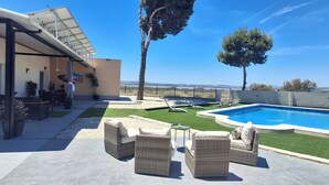 Un patio moderno al aire libre con piscina, mobiliario de mimbre y vistas al paisaje.
