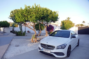 A white car parked in a driveway with a tree and a building in the background. - Villa Mi Atardecer (Torrevieja)