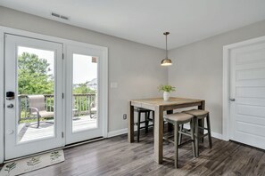Een kamer met een houten tafel, twee stoelen, een hanglamp en een deur die leidt naar een terras.