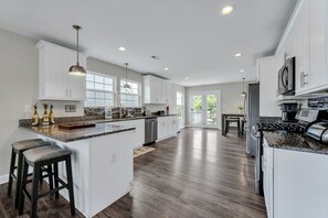 Een ruime keuken met witte kasten, een groot eiland en een eethoek met een tafel en stoelen.