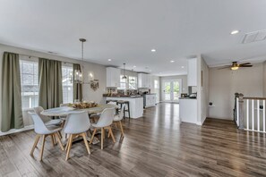 Een ruime keuken met witte kasten, een eethoek met een ronde tafel en stoelen, en een groot schiereiland.