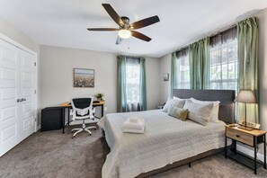 Ein Schlafzimmer mit Bett, Schreibtisch, Stuhl, Deckenventilator und Nachttisch.
