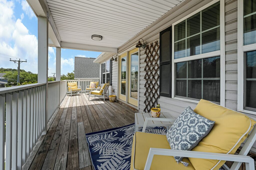 A covered porch with wooden flooring, white railings, and yellow cushioned chairs.