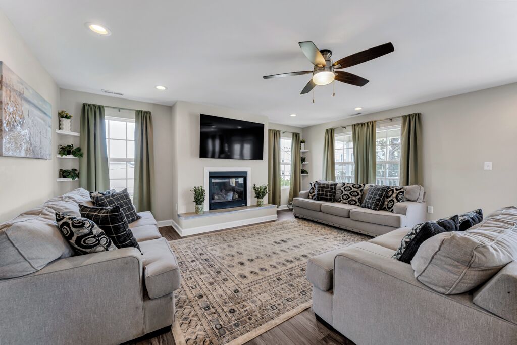 A living room with two sofas, a fireplace, a ceiling fan, and large windows.