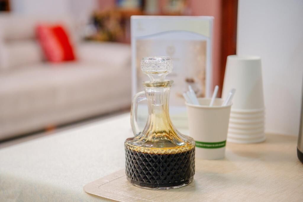 A glass decanter on a table with a cup holder and stacked cups.