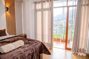 Une chambre à coucher avec un lit, une table de chevet, une fenêtre avec des rideaux et un balcon offrant une vue.