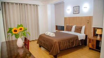A hotel room with a bed, a bedside table, a lamp, a picture on the wall, and a window with curtains.