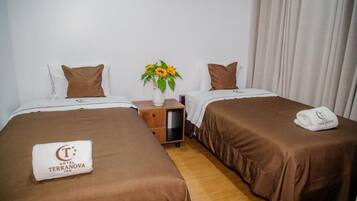 A hotel room with two beds, a nightstand, a vase with flowers, and a towel with the hotel logo.