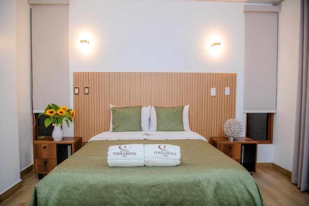 A hotel room with a bed, two nightstands, a wall-mounted TV, and a window with curtains.