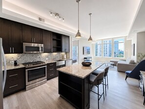A modern kitchen with dark cabinets, stainless steel appliances, and a large island. - Level Dallas Uptown (Dallas)
