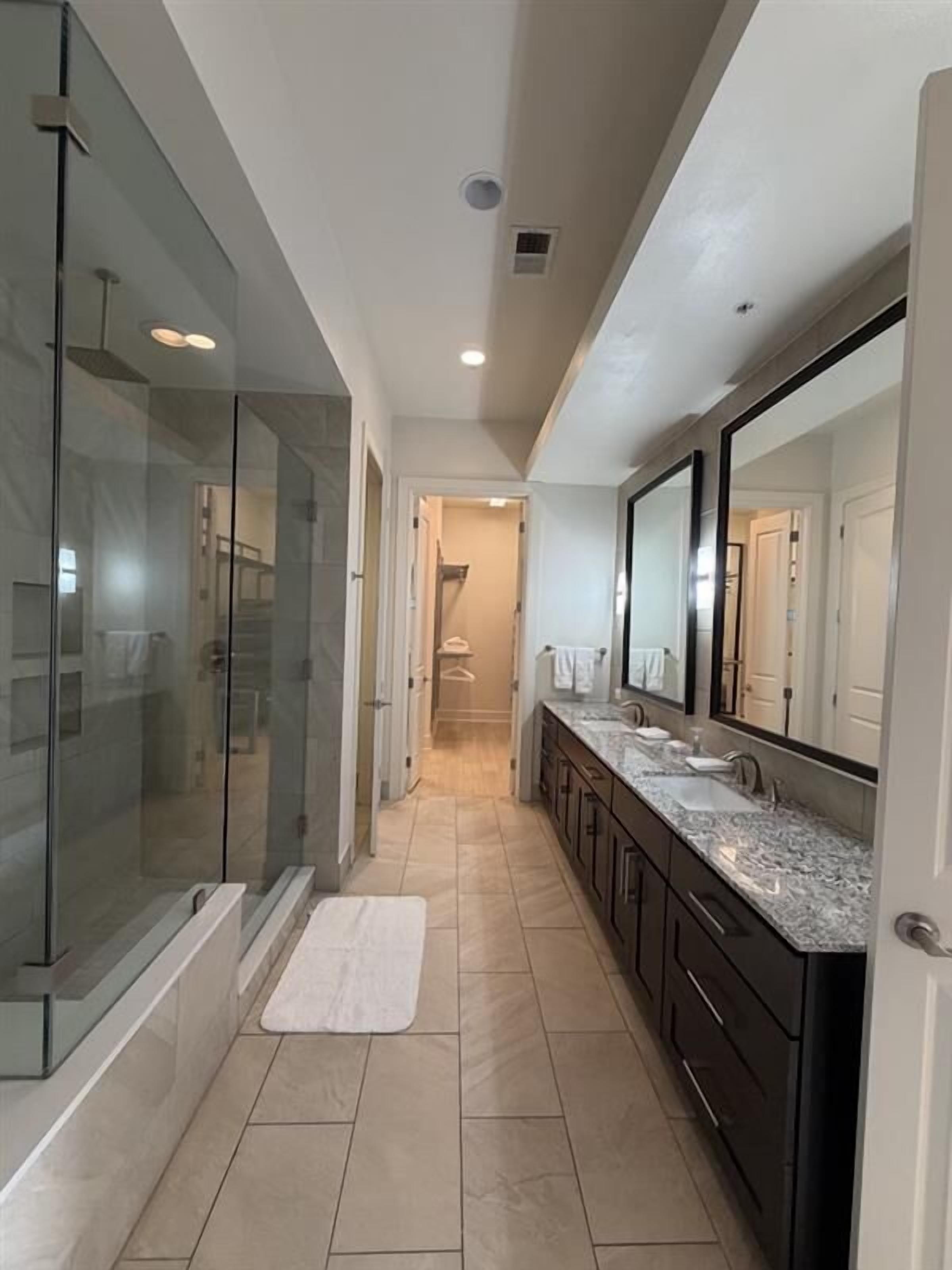 A modern bathroom with a glass shower enclosure, a vanity with a large mirror, and a tiled floor.