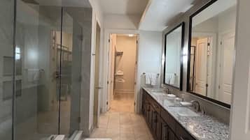 A modern bathroom with a glass shower enclosure, a vanity with a large mirror, and a tiled floor.