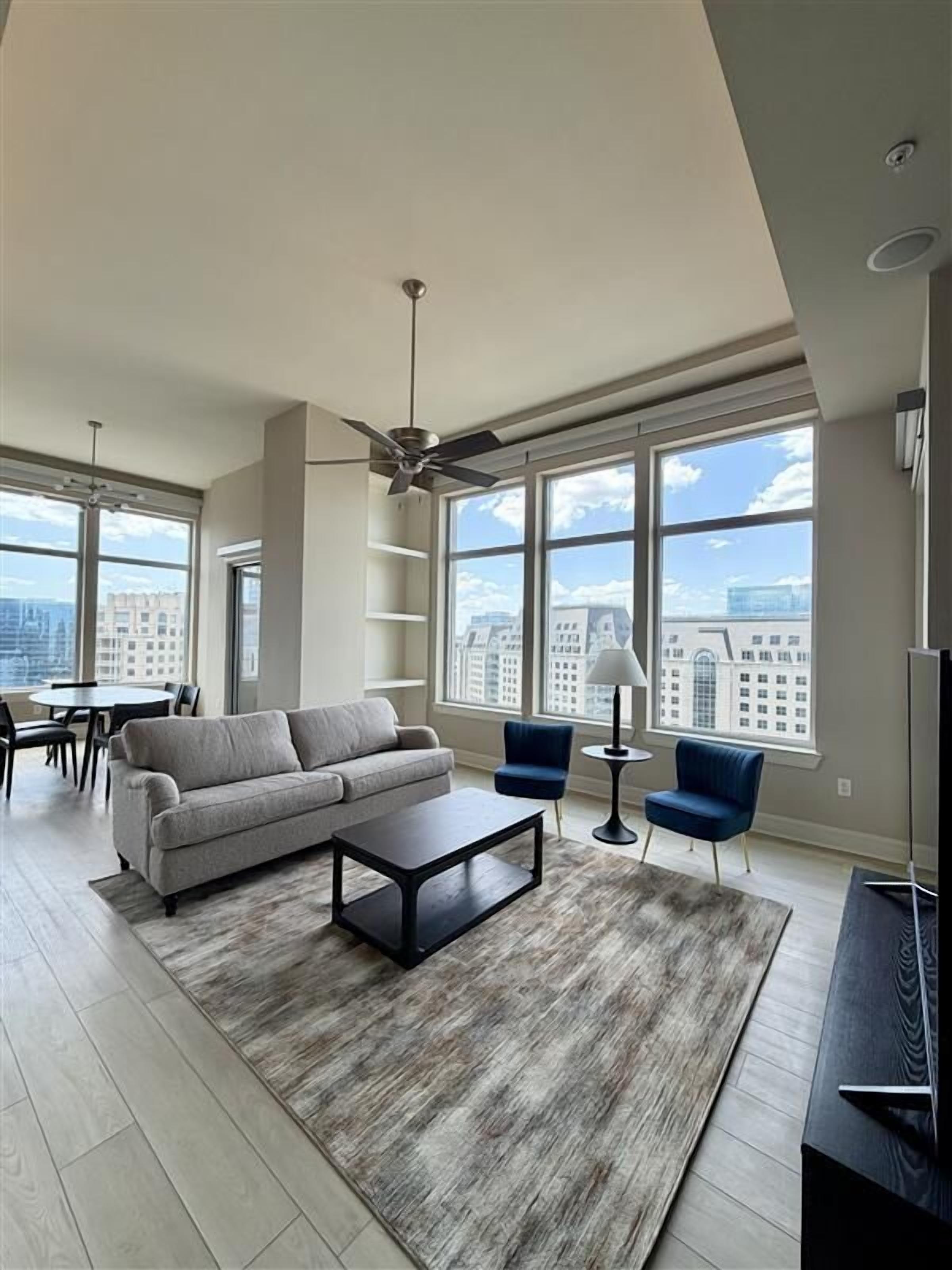A spacious living room with a large window, a ceiling fan, a sofa, a coffee table, and a TV.
