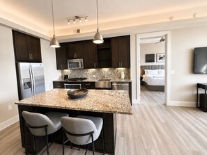A modern kitchen with dark cabinets, stainless steel appliances, and a granite island with bar stools. - Level Dallas Uptown (Dallas)