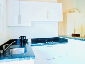 A kitchen with white cabinets, a black countertop, a stainless steel sink, and a coffee maker. - Endless Summer - by Zenbreak (Inch Marlowe)