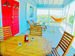 A covered patio with wooden furniture, a red door, and a hammock. - Endless Summer - by Zenbreak (Inch Marlowe)