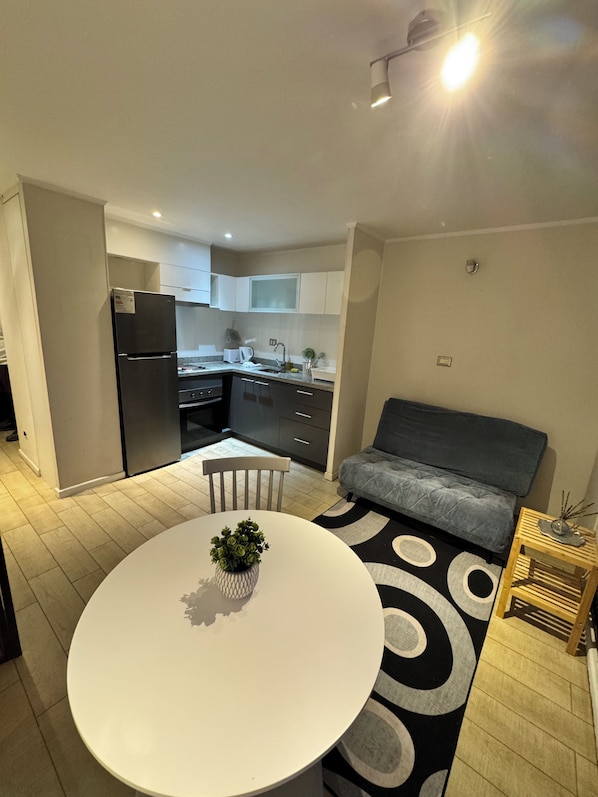 Una cocina moderna con armarios blancos, un refrigerador negro y una mesa de comedor con una planta en maceta.