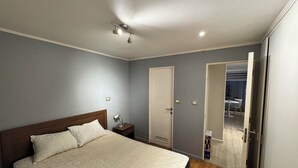Une chambre à coucher comprenant un lit, une table de chevet, une lampe et une porte donnant accès à une salle de bain.