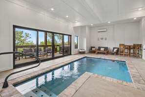 Une piscine dotée d’une terrasse ensoleillée, de chaises longues et d’une table avec des chaises.