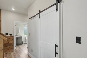 A hallway with a white door, a wooden staircase, and a bathroom with a sink and mirror. - Luxe Group Retreat | Pool, Theater, Views, Games (Sevierville)