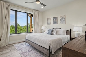 A bedroom with a large window, a bed, two bedside tables with lamps, and a wooden desk. - Luxe Group Retreat | Pool, Theater, Views, Games (Sevierville)