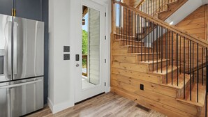 Una cocina moderna con un refrigerador de acero inoxidable, una puerta blanca y una escalera de madera con barandillas negras.