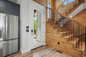 Une cuisine moderne avec un réfrigérateur en acier inoxydable, une porte blanche et un escalier en bois doté de rampes noires.