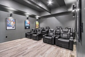 A home theater with black leather recliners, a wooden floor, and movie posters on the wall. - Luxe Group Retreat | Pool, Theater, Views, Games (Sevierville)