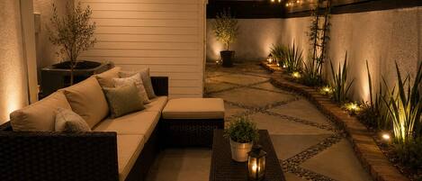 Un espace patio aménagé avec un canapé, une petite table ornée d’une plante et un chemin menant à un bâtiment.
