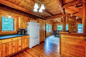 Interior de una cabaña de madera con cocina, comedor y ventanas amplias.