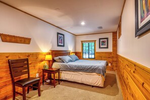 A bedroom with a bed, a chair, a bedside table, a window, and wooden paneling on the walls.