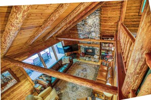 A cozy loft-style living area with a stone fireplace, leather sofas, and a wooden ceiling.