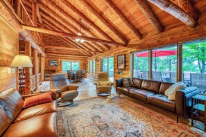 A log cabin interior with a fireplace, leather furniture, and large windows.