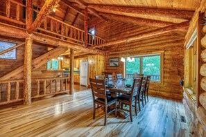 A log cabin interior with a dining area, kitchen, and a staircase.