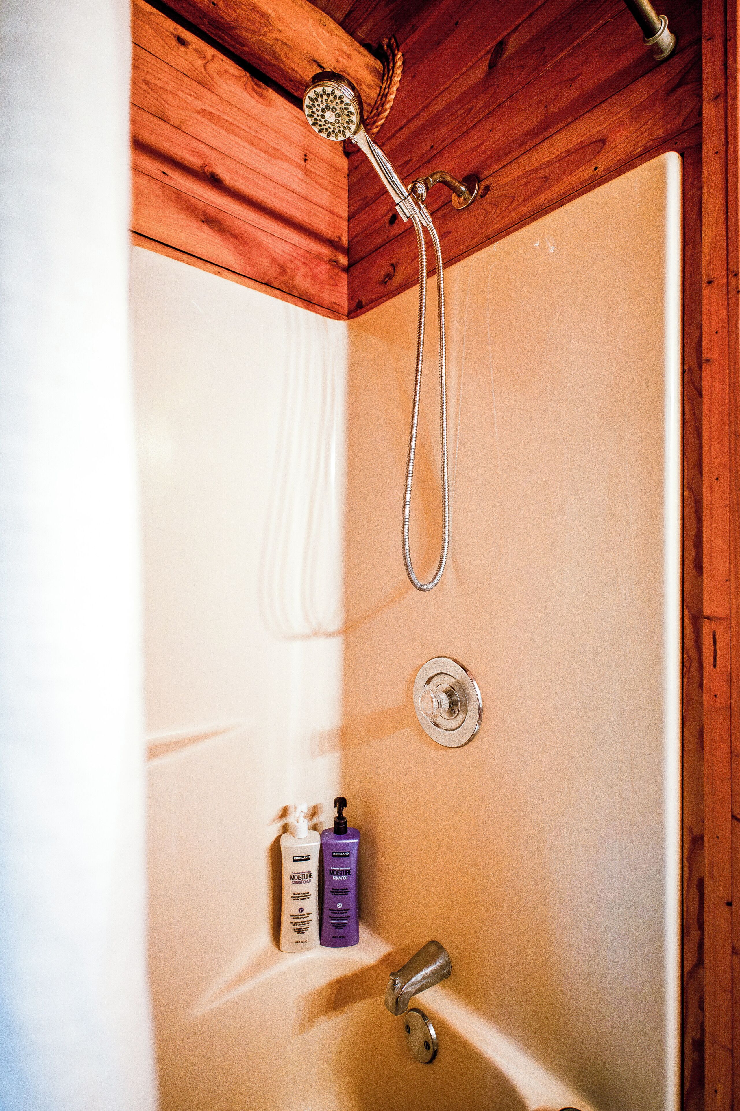 A shower with a handheld showerhead, a wall-mounted faucet, and two bottles of Kirkland Moisture Conditioner and Shampoo.