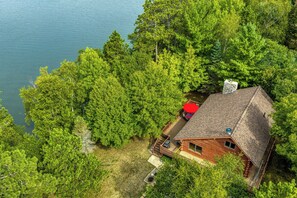 Una cabaña con terraza, rodeada de un bosque denso y un lago.