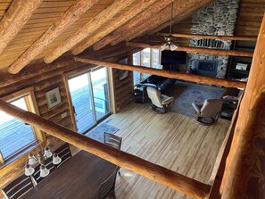 Ein geräumiges Loft mit hohen Decken, Holzbalken, einem Steinkamin, einem großen Fenster und einer gemütlichen Sitzecke.