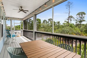 Une véranda abritée avec une table et des chaises, un ventilateur de plafond et une vue sur les arbres et la verdure.