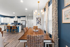 Une cuisine moderne avec des meubles blancs, un îlot central et un coin repas comprenant une table en bois et des chaises en osier.