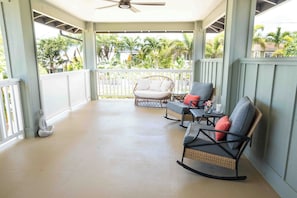 A covered porch with wicker chairs, a small table, and a decorative Buddha statue. - Welcoming 4-bedroom beach house with AC in Ewa Beach (Ewa Beach)