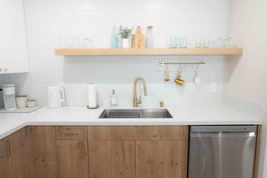 A kitchen with a stainless steel sink, wooden cabinets, a white countertop, and a dishwasher. - Welcoming 4-bedroom beach house with AC in Ewa Beach (Ewa Beach)