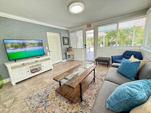 A living room with a TV, white entertainment unit, glass coffee table, sofa, and patterned rug. - Private Pool + Mini Golf | Near Hollywood Beach (Hollywood)
