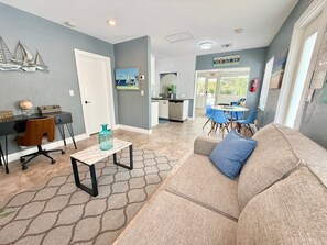 A living room with a sofa, a coffee table, a desk, and a dining area with chairs.