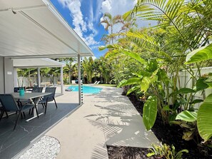 A covered patio area with a pool, outdoor seating, and lush tropical vegetation.