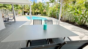 Een overdekte terras met een zwembad, ligstoelen en een tafel met een waterfles.