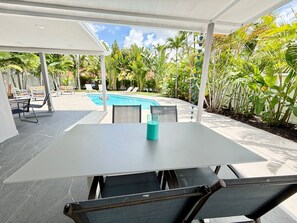A covered outdoor patio with a pool, lounge chairs, and a table with a water bottle. - Private Pool + Mini Golf | Near Hollywood Beach (Hollywood)