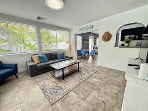Ein modernes Wohnzimmer mit einer Couch, einem Couchtisch und Sesseln. An der Wand befindet sich ein Schild mit der Aufschrift 'BEACH HOUSE'.