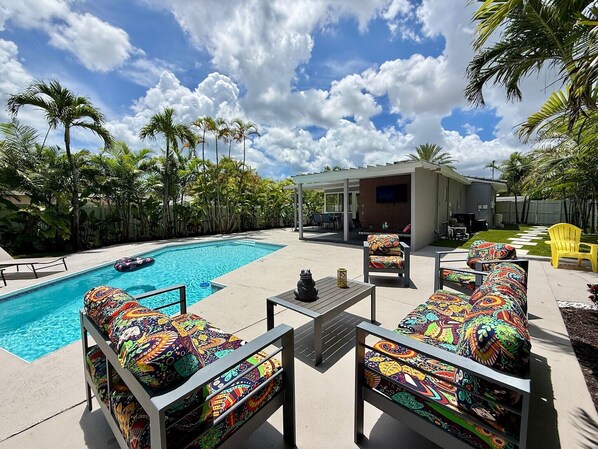A pool area with colorful lounge chairs, a small table, and a covered patio.