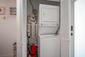 A laundry room with a front-loading washer and dryer, a red bucket, and a water heater.